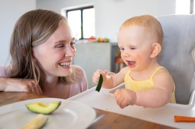 Joyful mom watching baby eating solid food