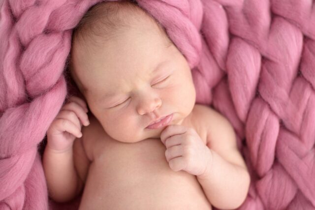 sleeping newborn girl on coral pink background