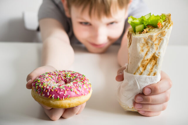 Junk food and child concept. Teen boy holding a donut in the icing and shawarma sandwich roll