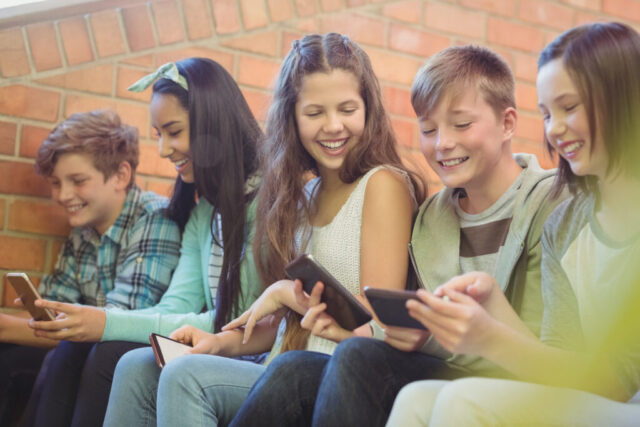 Group of smiling school friends sitting on staircase using mobile phone
